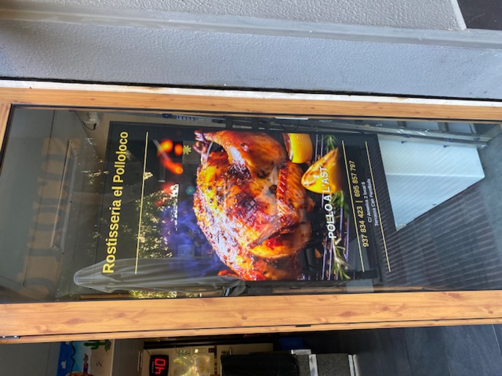 Pantalla vertical de Lokally instalada en la entrada de El Pollo Loco, vista desde dentro del local hacia la calle